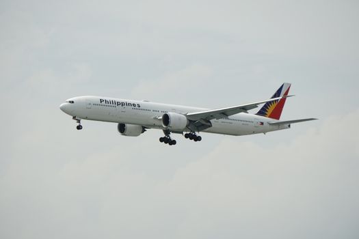 Boeing 777 of Philippine Airlines flying against a cloudy sky.