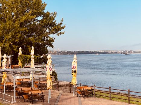 Tranquil view of deserted riverside café with closed yellow umbrellas on a sunny day.