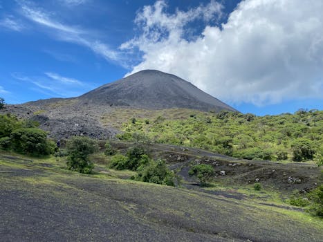 Lush green landscape with Pacaya Volcano under a blue sky in Guatemala.