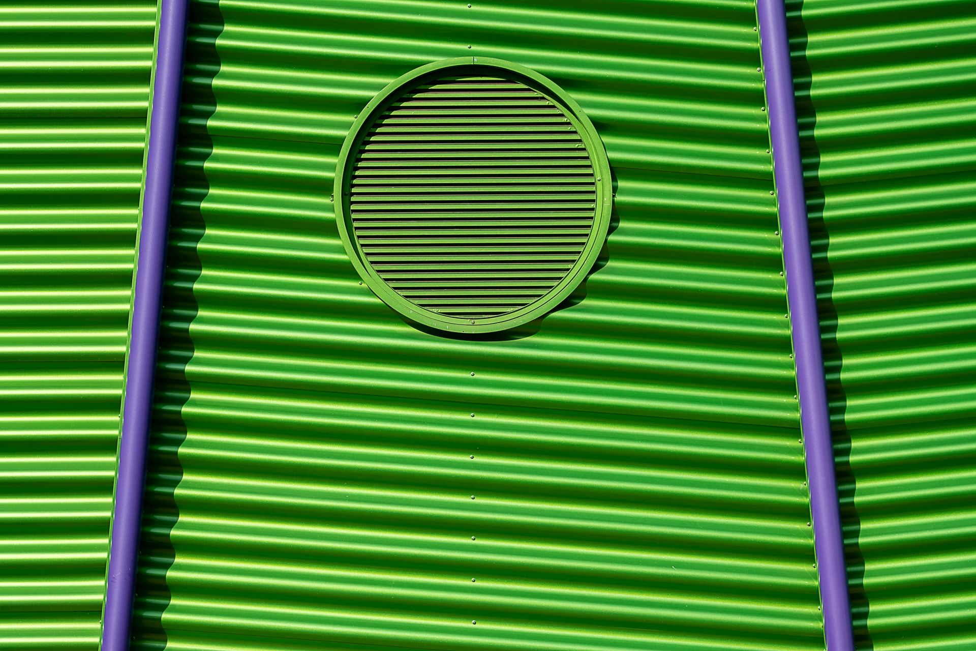 Vivid green corrugated metal wall featuring a circular vent and purple accents, creating a striking visual contrast.