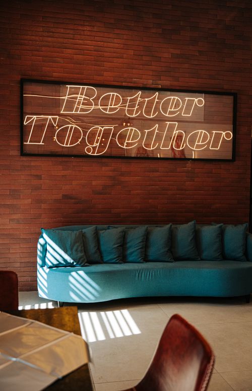 Free Cozy lounge with teal sofa and 'Better Together' neon sign, earthy tones enhance the modern ambiance. Stock Photo