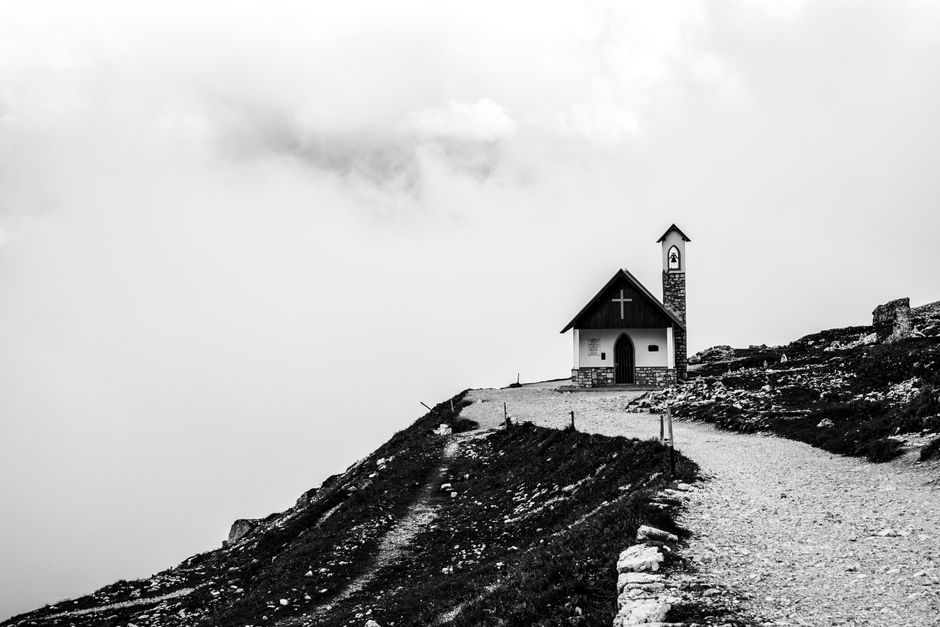 Black and white photo of a solitary chapel on a mountain path in misty weather.