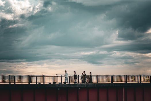 Group of people walking on a bridge under a dramatic cloudy sky, creating a cinematic scene.