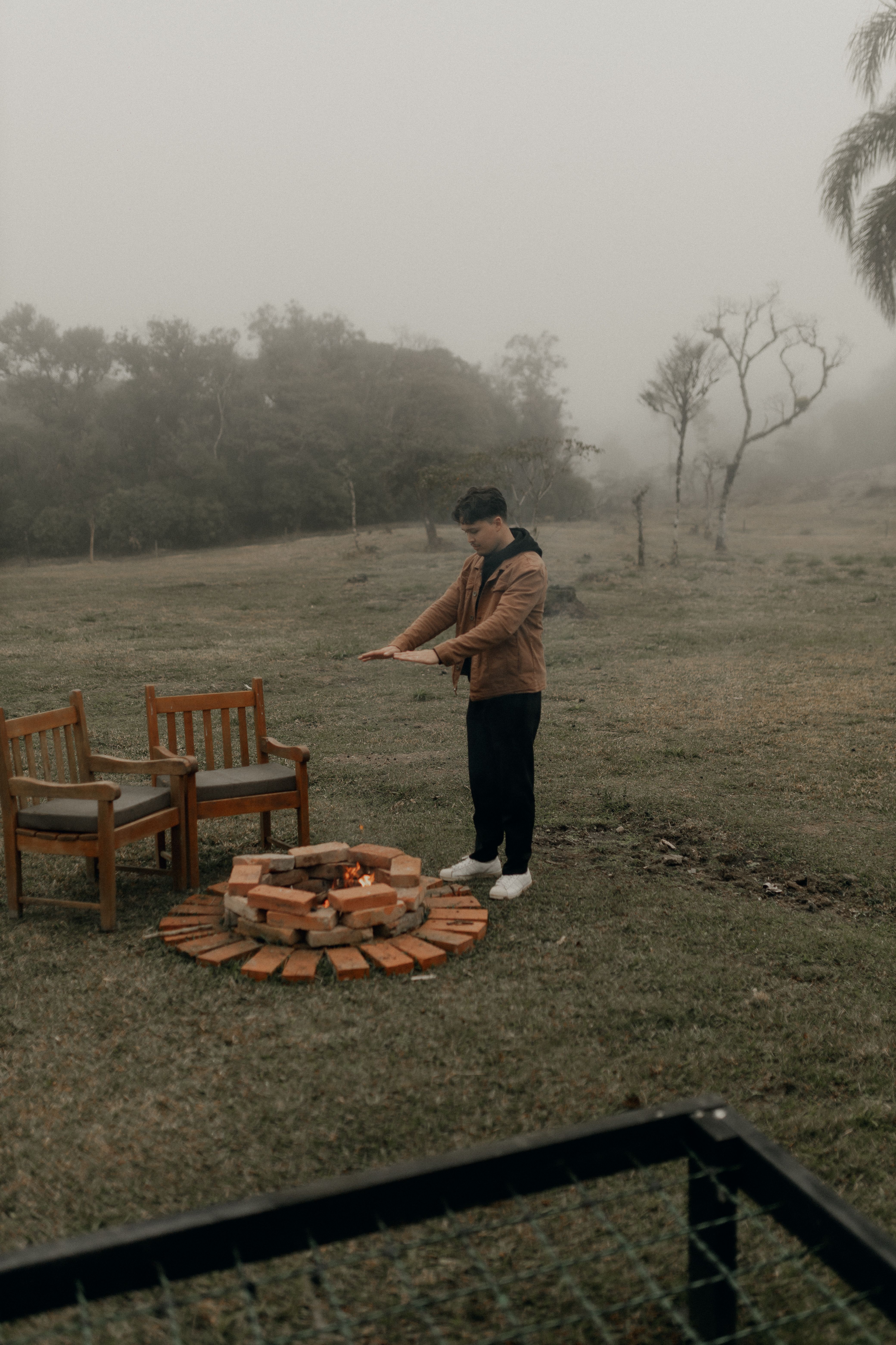 A person warming hands by a campfire on a misty day in the outdoors.