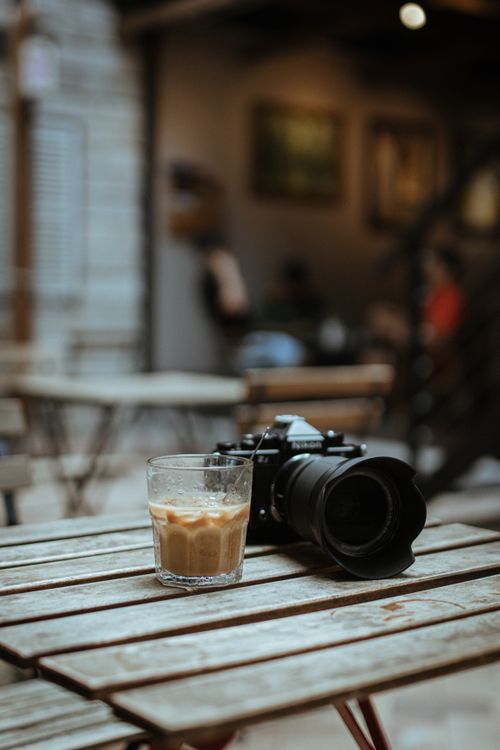 Free A camera and iced coffee rest on a rustic table in an atmospheric cafe setting. Stock Photo