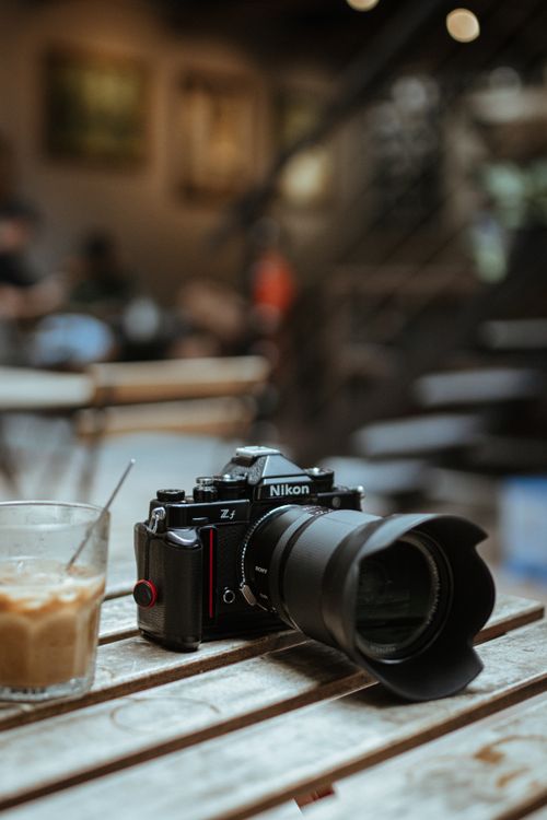 Free A close-up of a camera and iced coffee on a rustic outdoor cafe table. Stock Photo