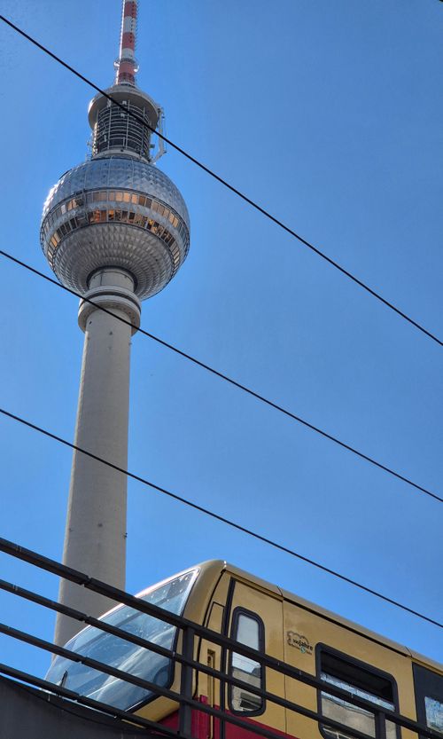 Free A dynamic capture of Berlin's TV Tower and a commuter train under a clear blue sky. Stock Photo