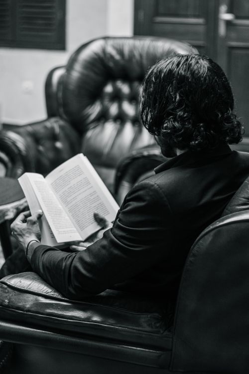 Free Man reading a book in a leather chair, captured in black and white for a classic look. Stock Photo