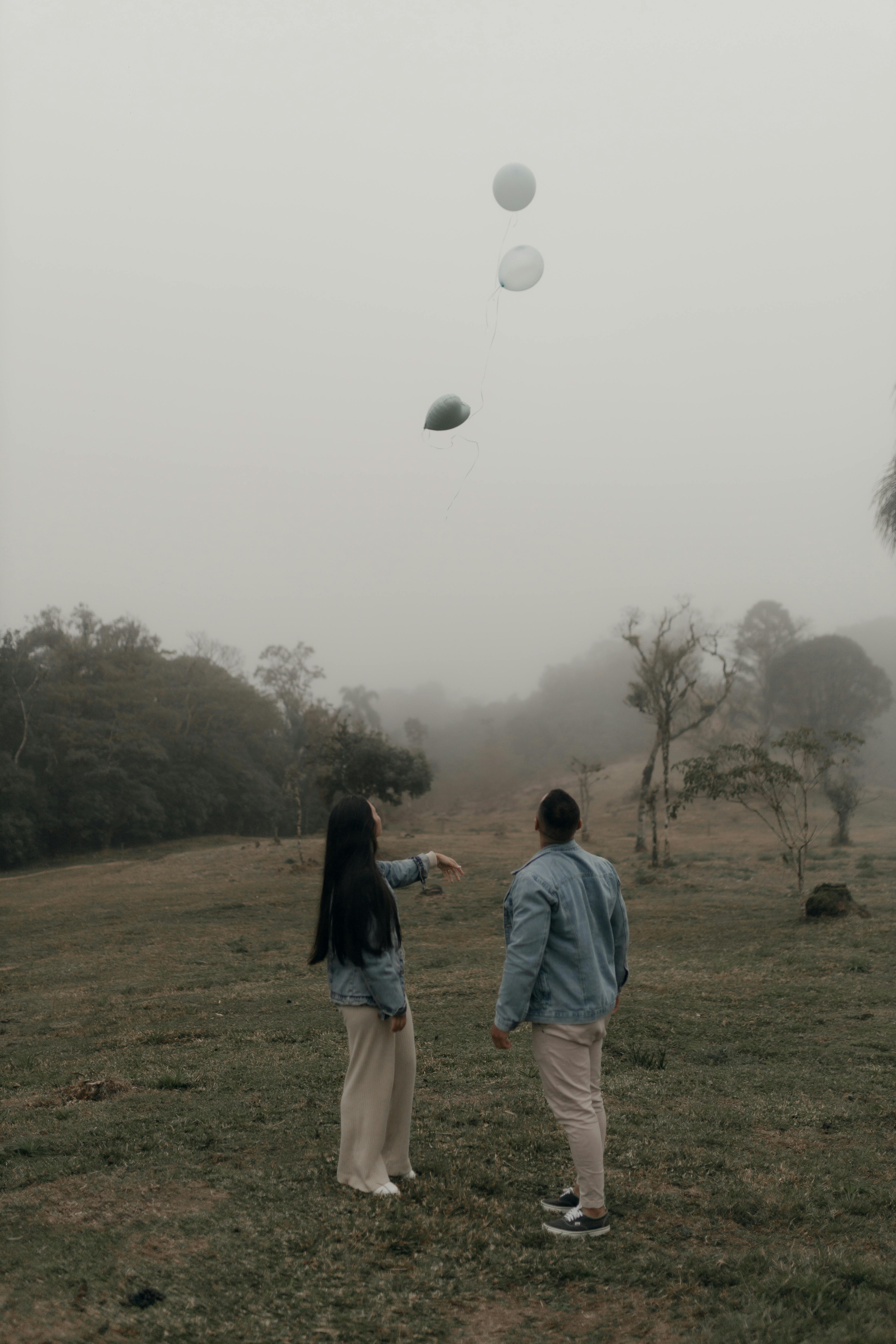 A couple lets go of balloons in a misty field, symbolizing freedom and serenity.