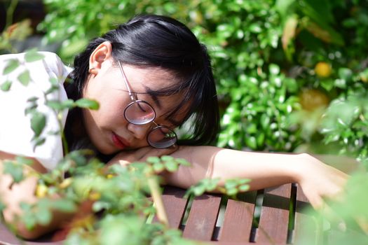 A young woman with glasses relaxes on a wooden table in a lush garden setting, surrounded by greenery.