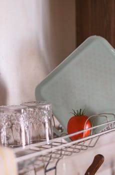 Cozy kitchen scene with a fresh tomato on a drying rack beside glassware.