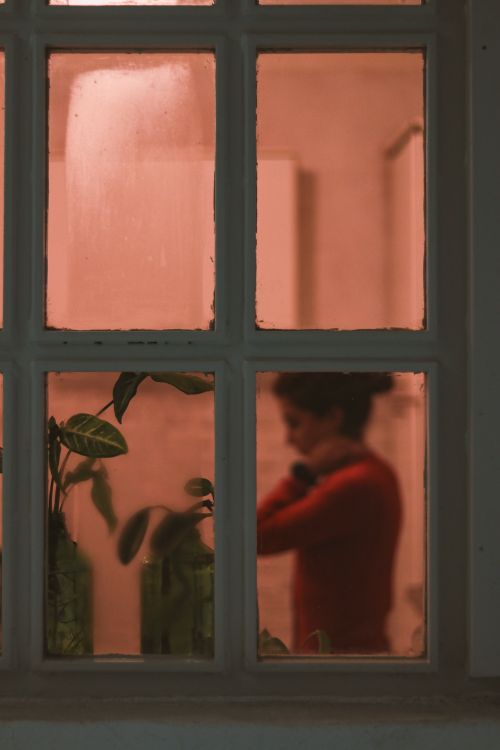 Free Silhouette of a woman through a window with warm indoor light, creating a cozy atmosphere. Stock Photo