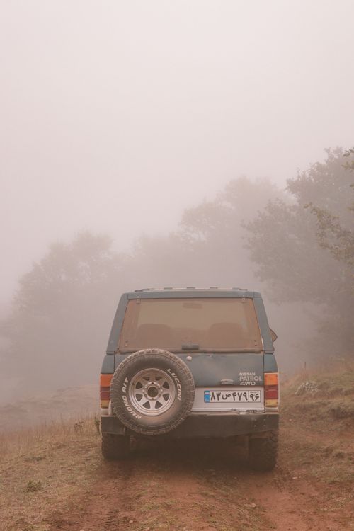 Free An off-road vehicle parked on a foggy dirt path surrounded by nature, creating a mysterious atmosphere. Stock Photo