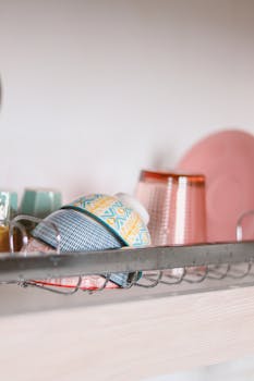 A collection of vibrant bowls and glasses on a kitchen shelf, showcasing cozy home decor.