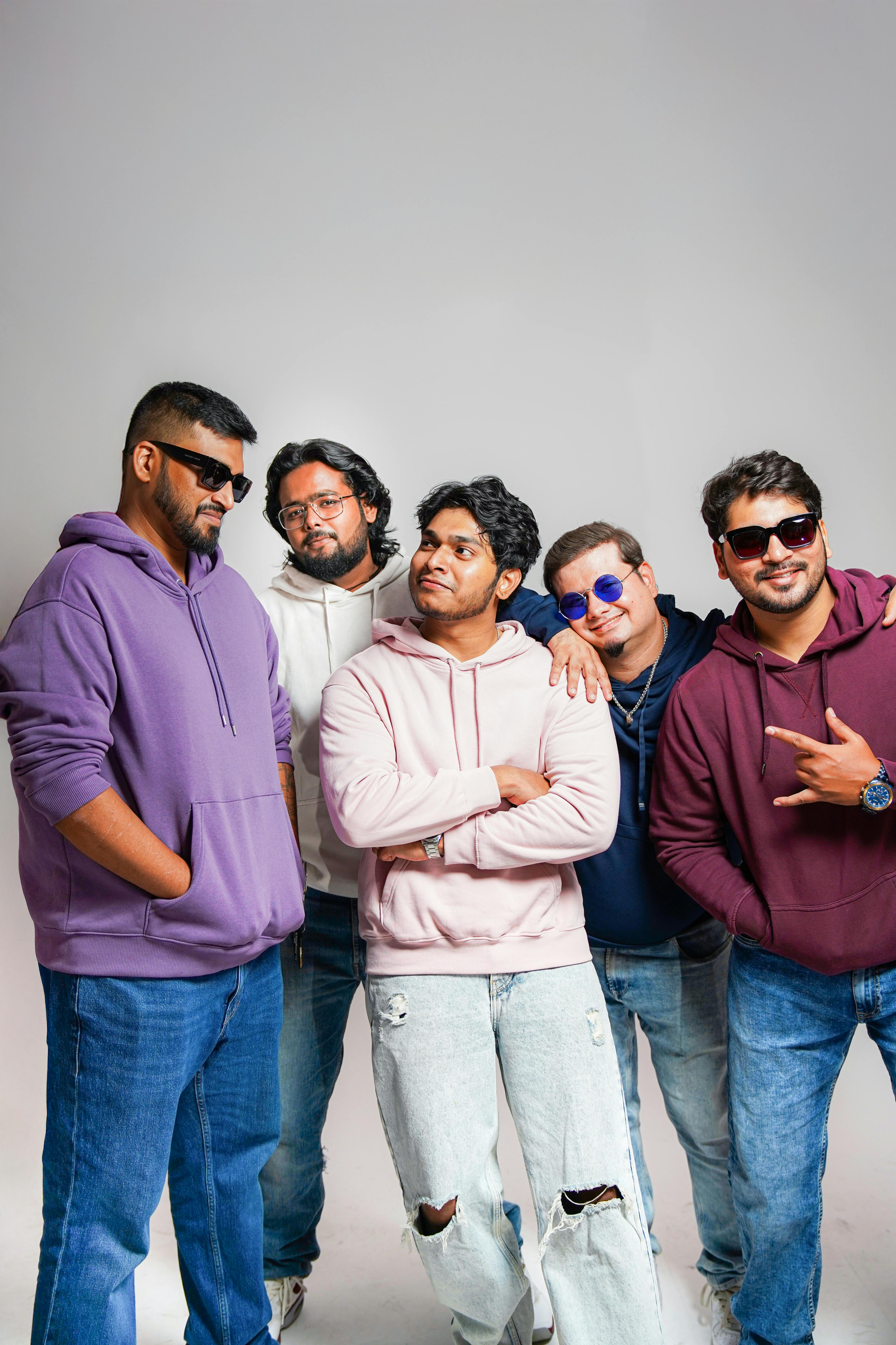 A group of adult friends posing casually in a studio setting, wearing colorful hoodies and sunglasses.