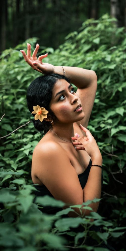 Free A woman gracefully poses amidst lush green foliage, exuding elegance and natural beauty. Stock Photo