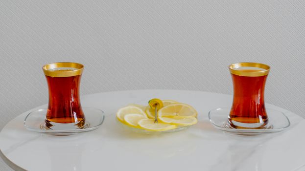 Two tea glasses with lemons on a white marble table in a minimalist setting.