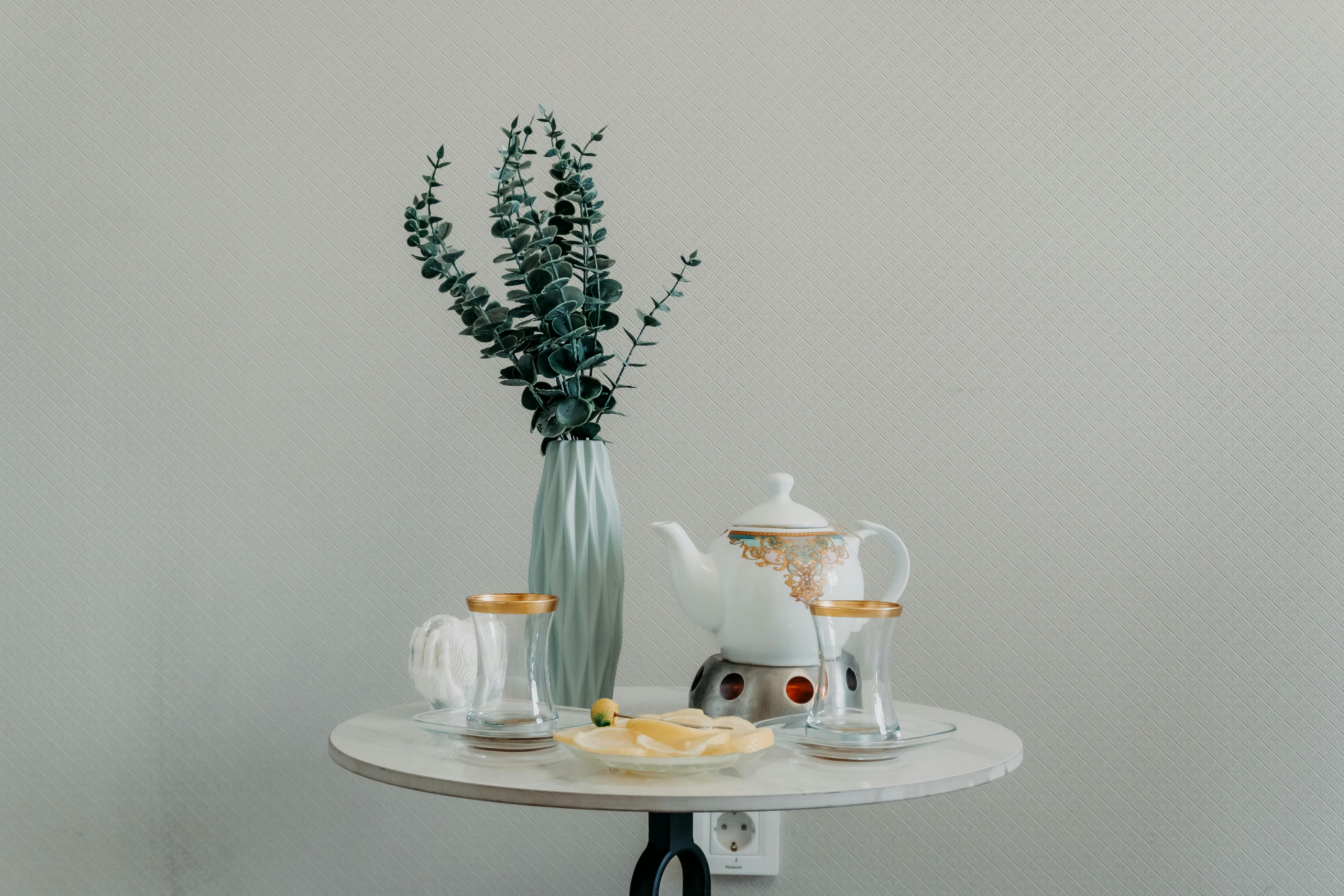 A minimalist tea setting on a round table with eucalyptus leaves in a vase, creating a peaceful ambiance.