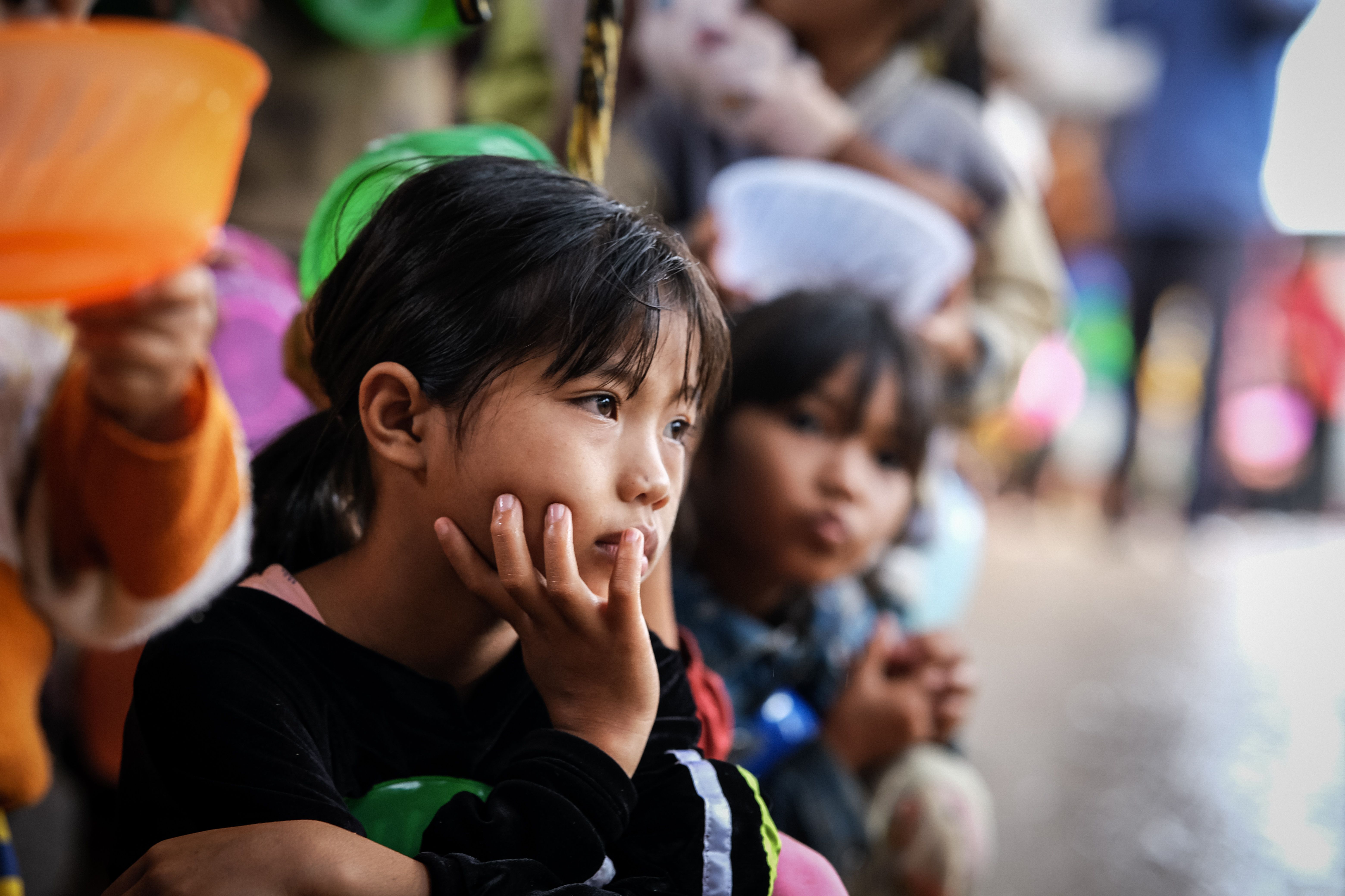 A young child gazes thoughtfully in a busy, vibrant outdoor market scene.