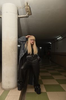 Stylish woman in leather pants poses in an underground corridor, creating a dramatic mood.