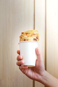A hand holding a cup with artisan bread, perfect for creative food presentations. Minimalist and warm.