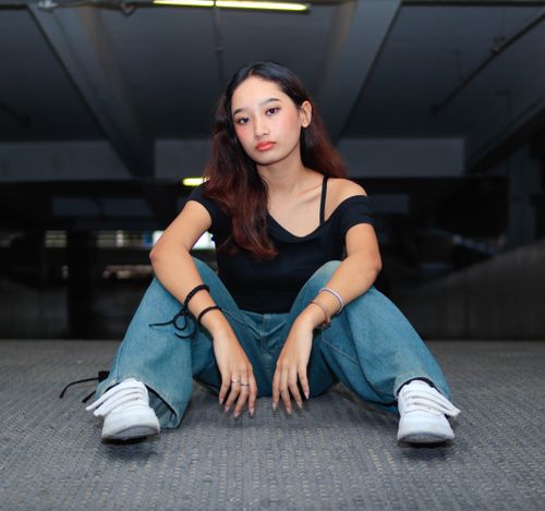 Free Portrait of a young woman sitting confidently in an urban parking garage, wearing casual attire. Stock Photo