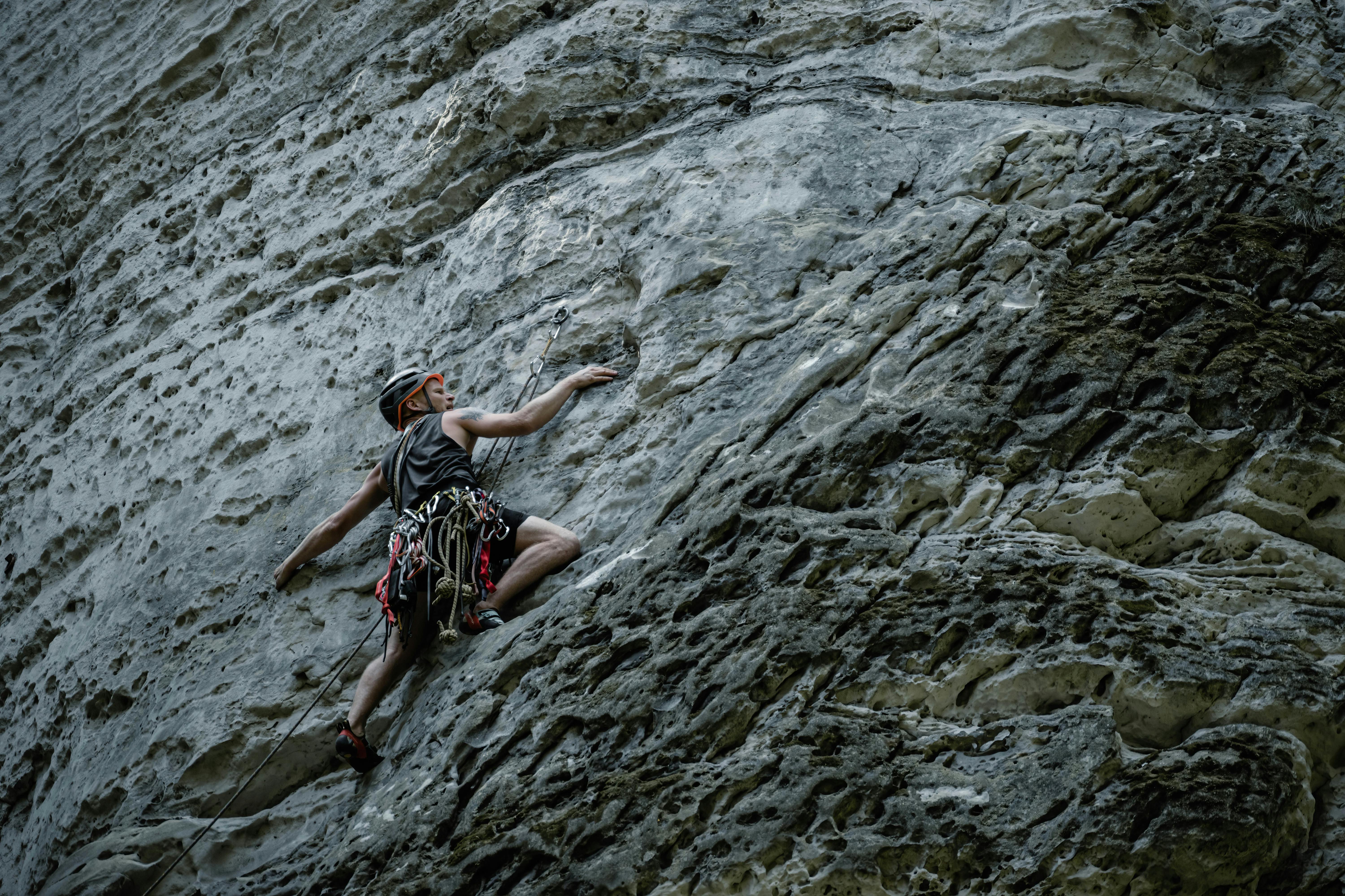 A determined rock climber in Česko ascends a rugged sandstone cliff face, showcasing strength and adventure.