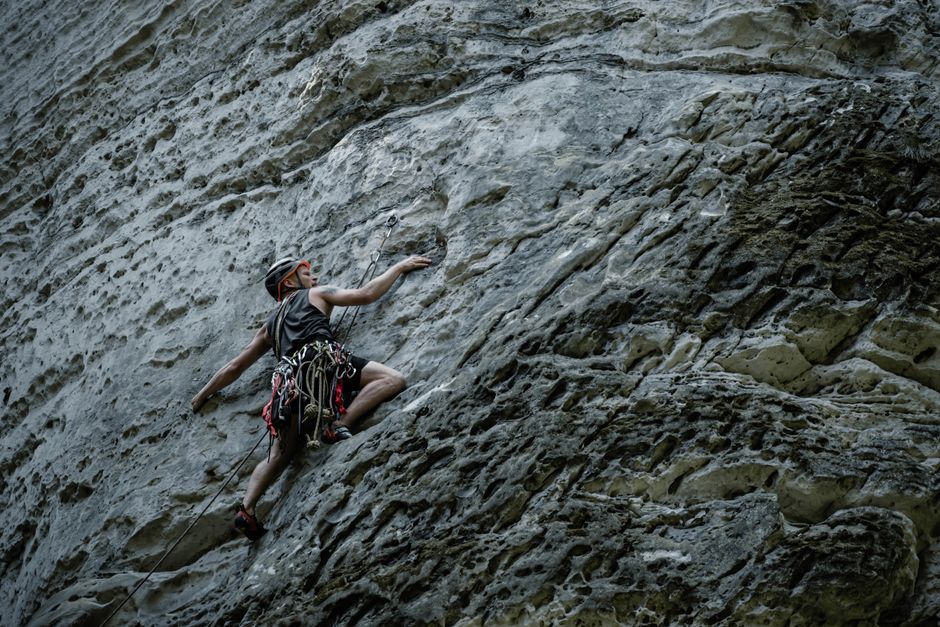 A determined rock climber in Česko ascends a rugged sandstone cliff face, showcasing strength and adventure.