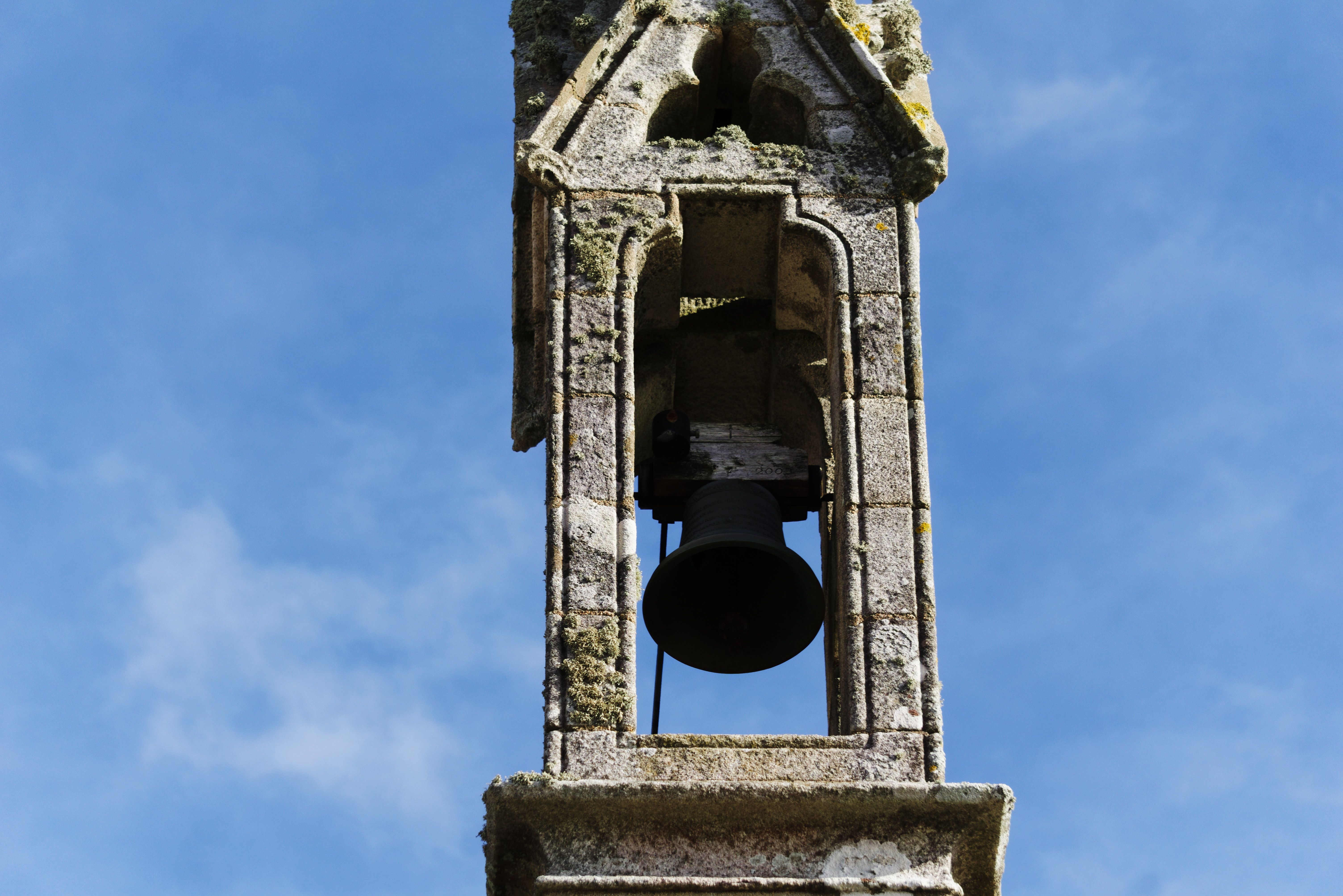A rustic stone chapel bell tower stands under a clear blue sky, symbolizing heritage and spirituality.