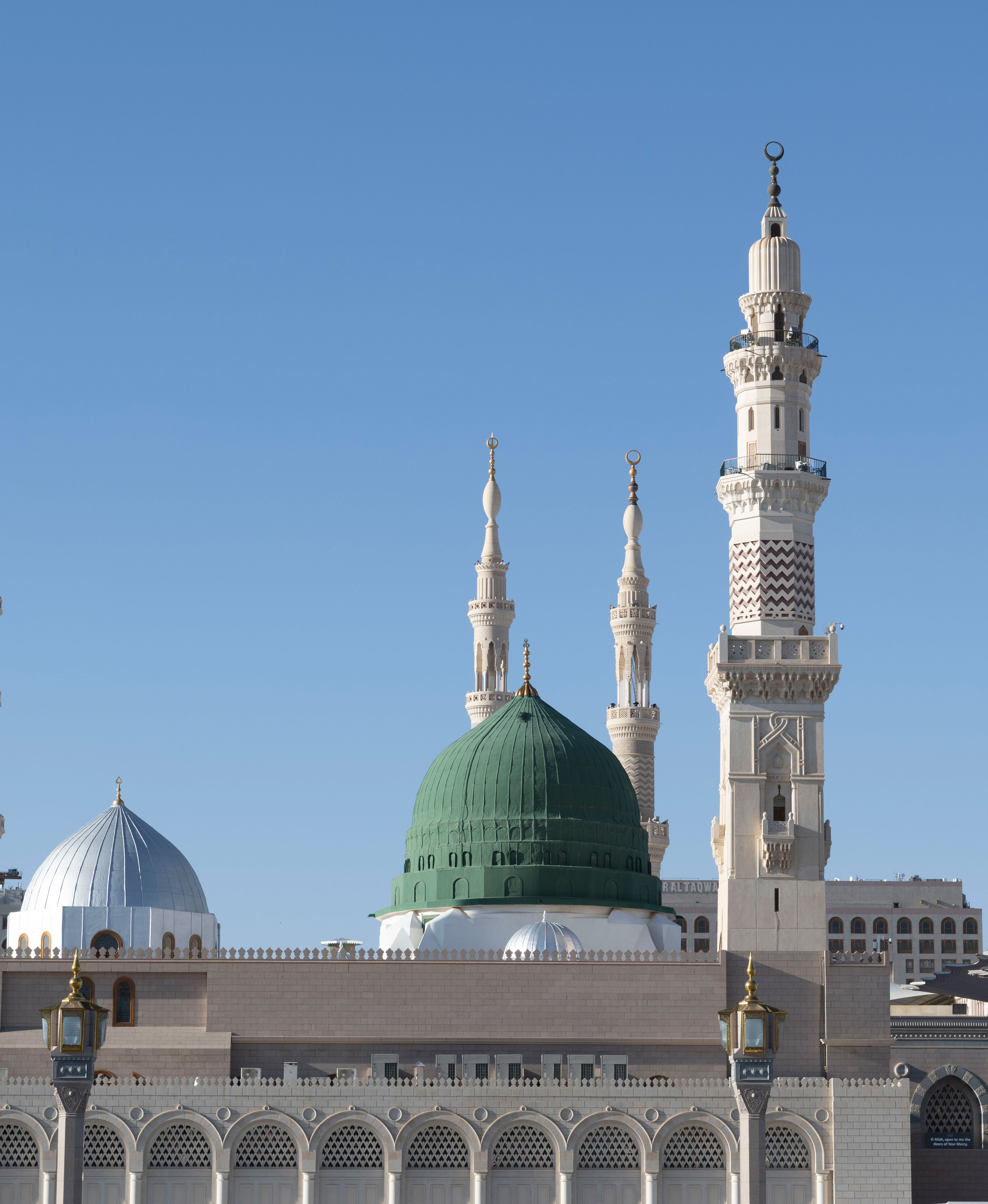 Vista cercana de la Cúpula Verde en la Mezquita Del Profeta ﷺ en Medina, Arabia Saudí, con los alminares alrededor sobre un cielo azul.