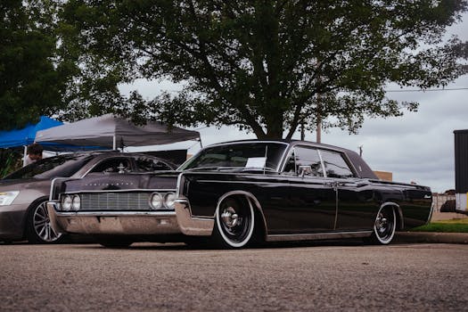 Vintage Lincoln Continental showcased in an outdoor car exhibition, under trees.
