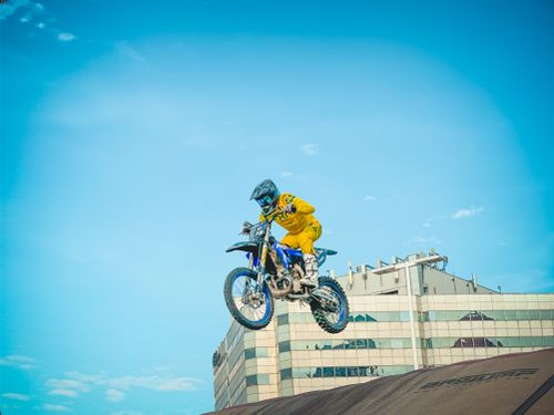 Free Exciting motocross stunt with rider in vibrant yellow gear jumping high against a city backdrop. Stock Photo