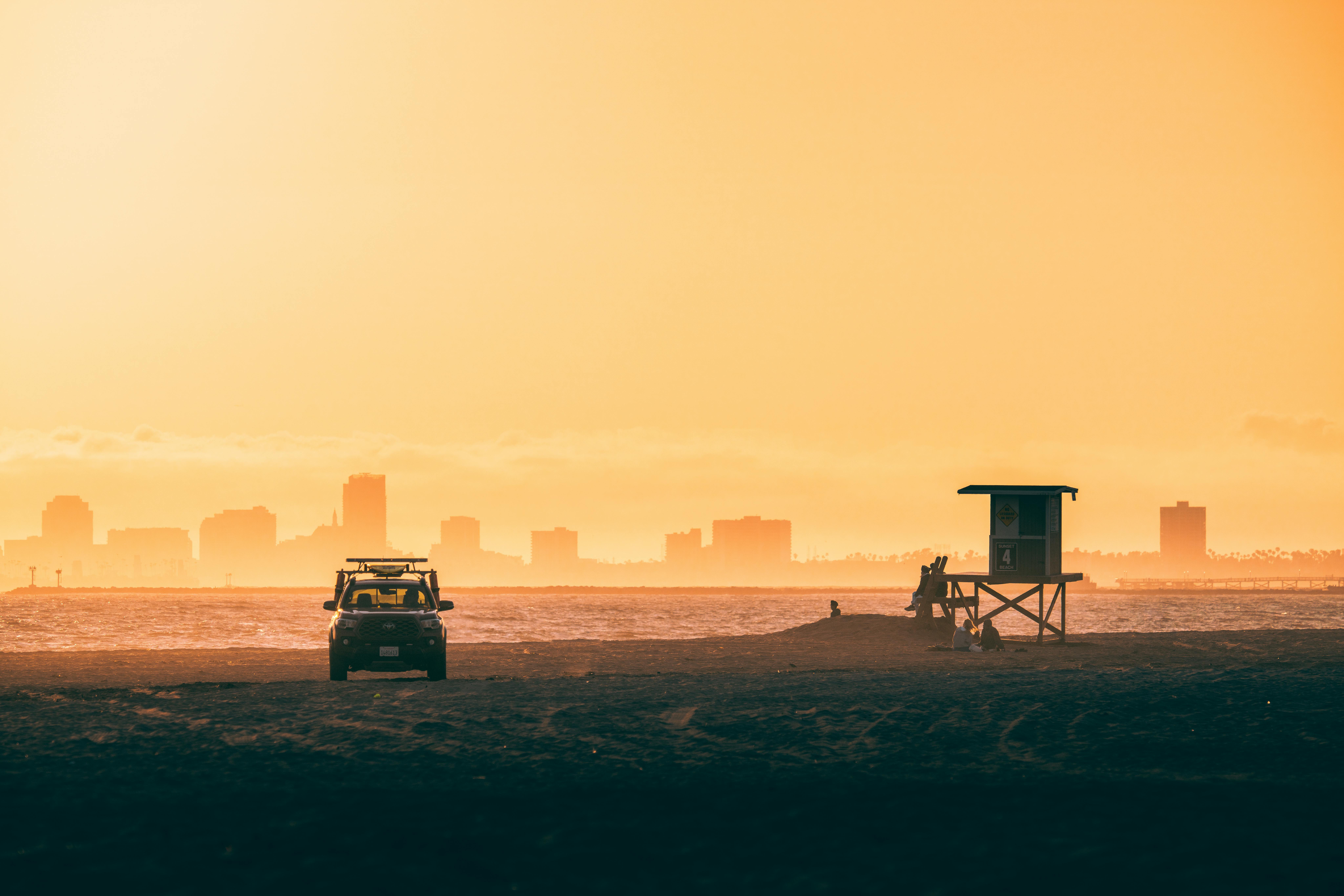 A serene beach during sunset with a lifeguard tower and city skyline in the background, exuding a warm, tranquil atmosphere.