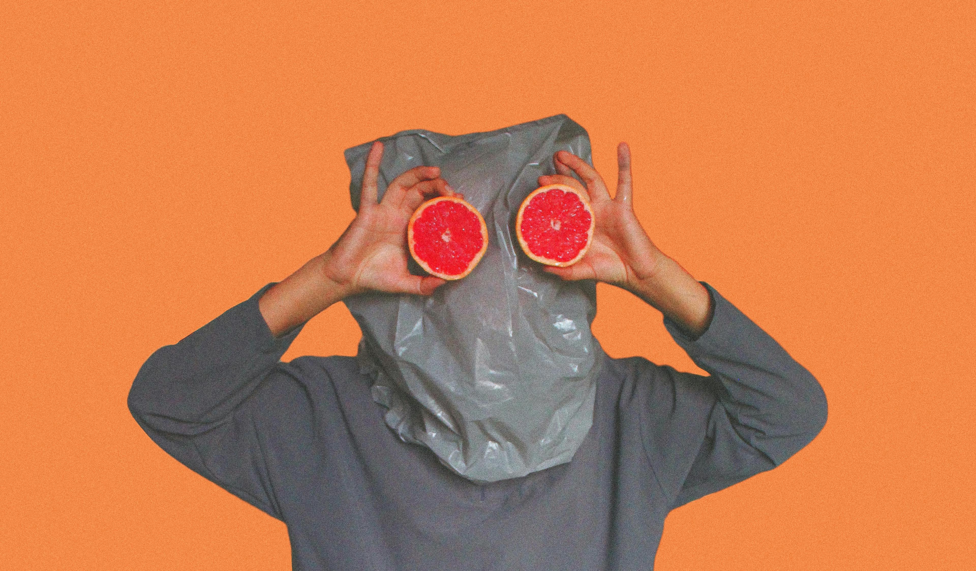 person covered with plastic bag on head while holding sliced blood orange