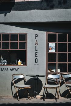 Cozy urban coffee shop exterior with take-away window and rustic chairs.