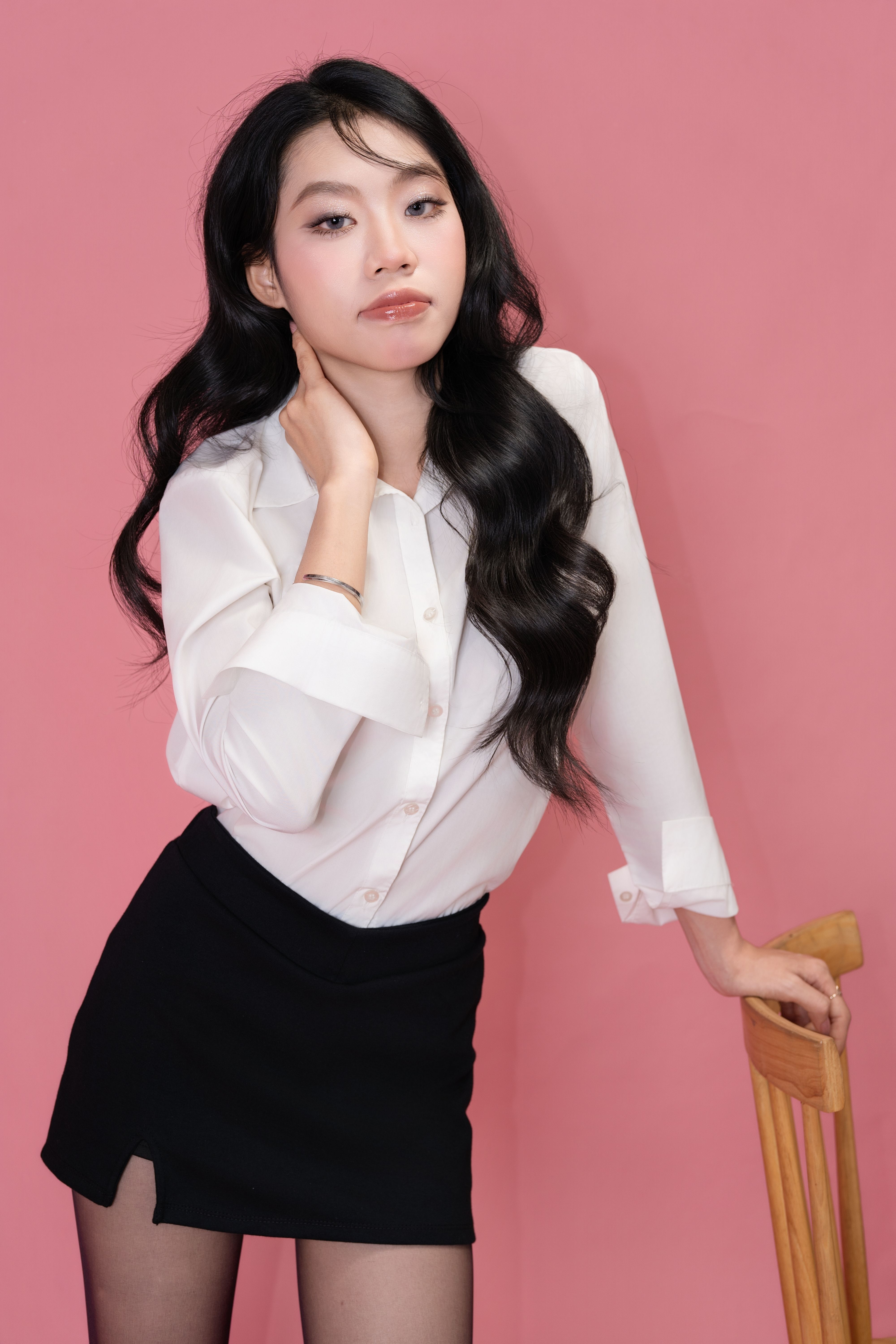 Stylish woman in white blouse and black skirt poses confidently on a pink backdrop.