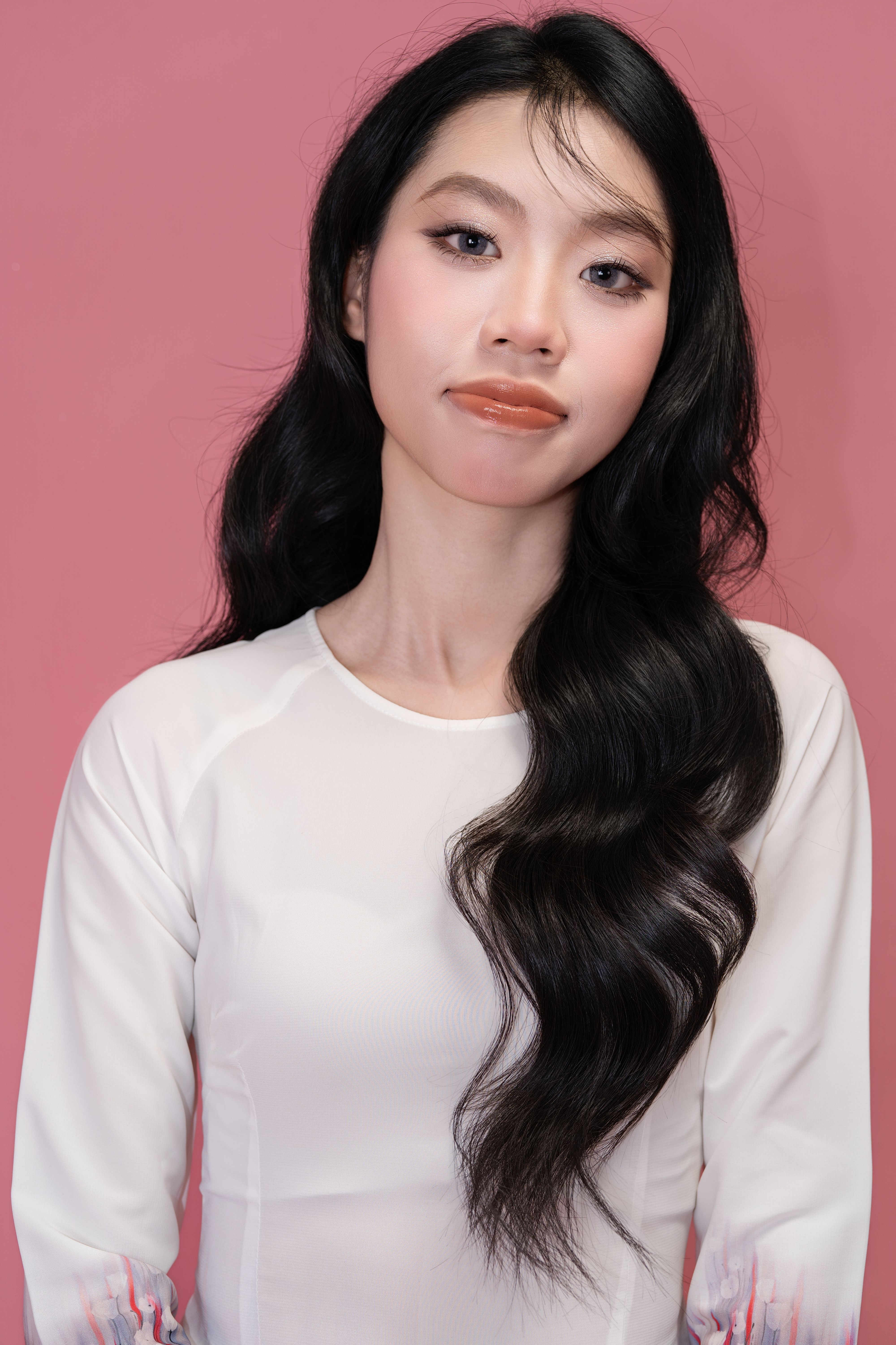 Stylish portrait of a woman with long black hair on a pink background, wearing a white top.