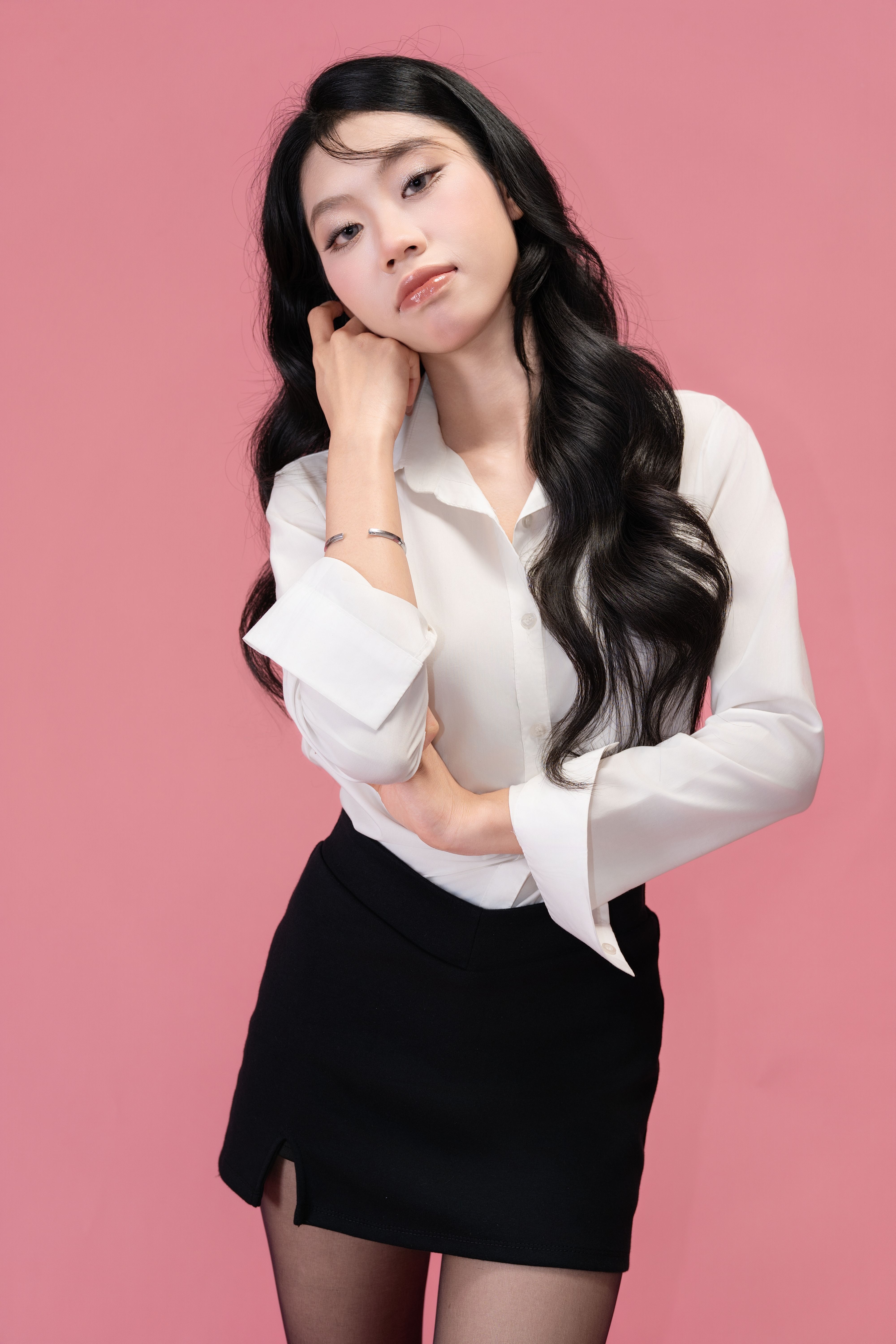 Stylish woman in white blouse and black skirt posing confidently with a pink backdrop.