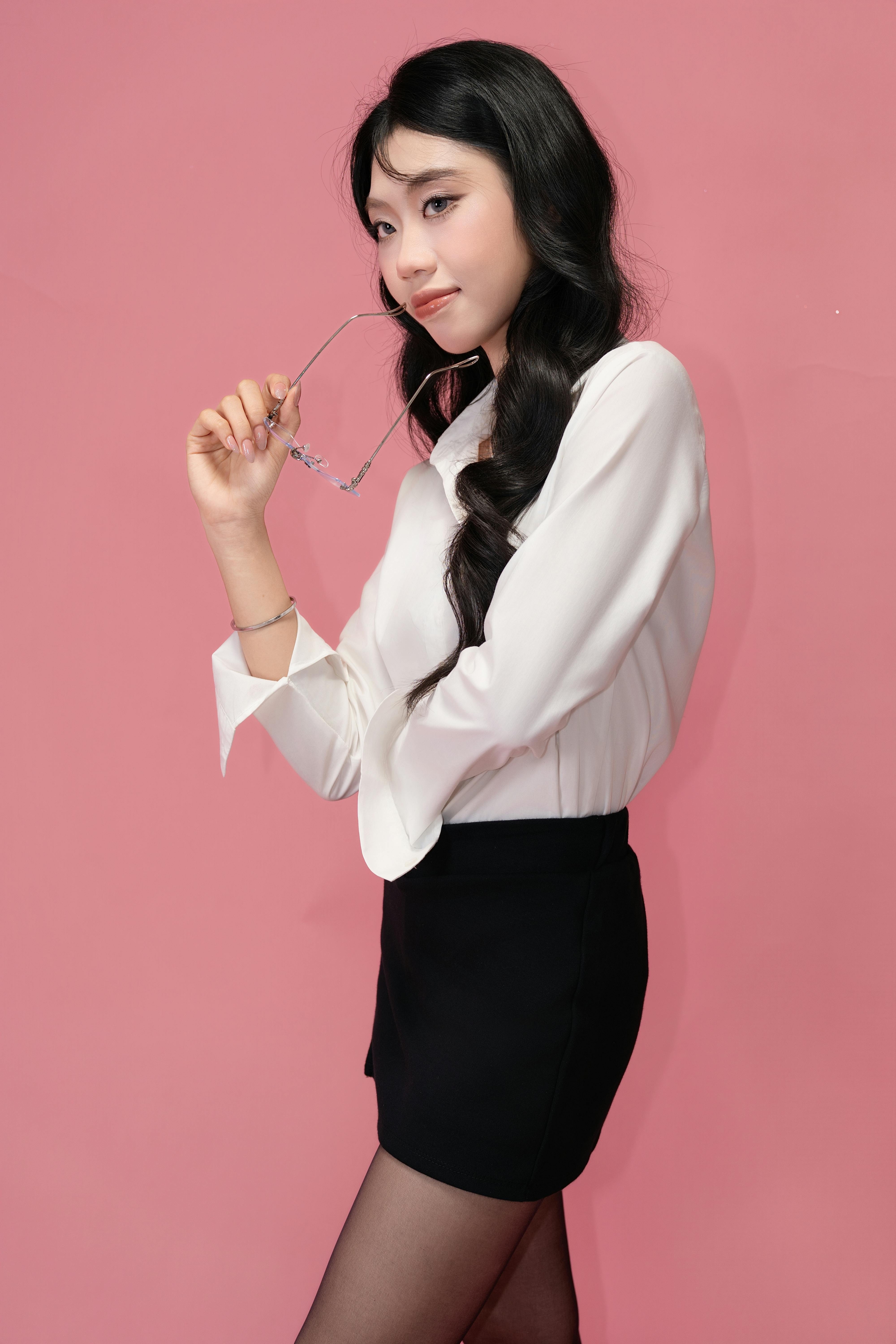 Free Stylish woman in formal attire posing with confidence against a pink backdrop. Stock Photo