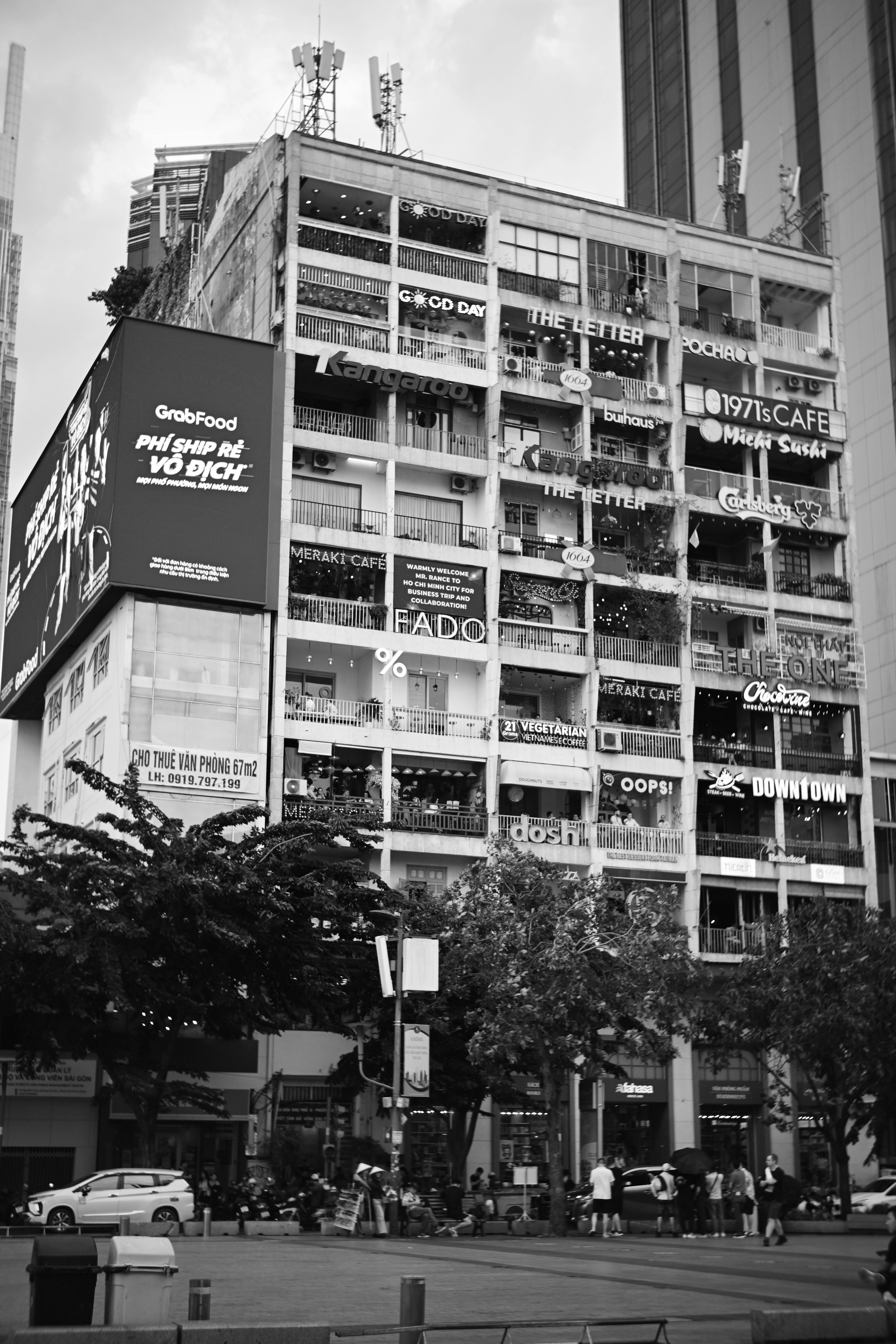 Black and white urban view of a multi-story building with cafes in a bustling city.