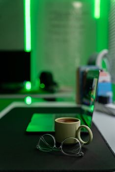 Modern office setup with a laptop, coffee mug, and decorative green lighting.