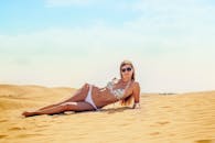 一位穿着比基尼、戴着太阳镜的女人在沙丘上享受阳光明媚的日子