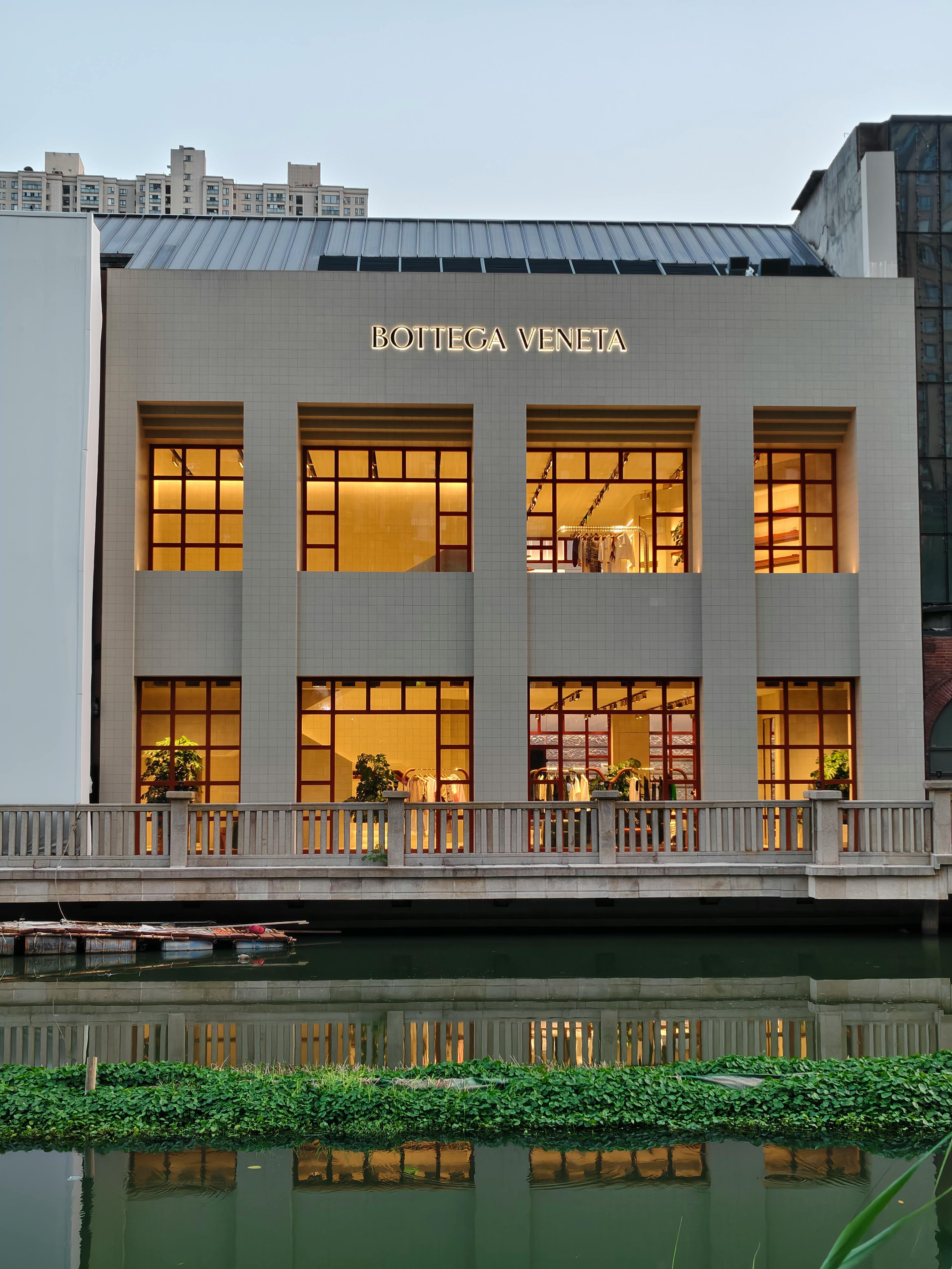 Ücretsiz Alacakaranlıkta suya yansıyan modern Bottega Veneta vitrini, lüks mimariyi sergiliyor. Stok Fotoğraflar