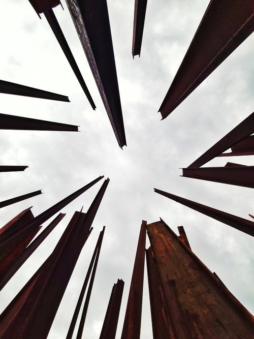 Free Dynamic view of rusted steel beams reaching towards an overcast sky, creating an abstract pattern. Stock Photo