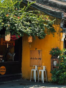 Rustic yellow wall with hanging lanterns and potted plants in a quaint outdoor setting.