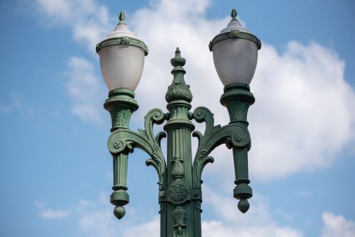 Free Artistic capture of a vintage street lamp with ornate design against a bright blue sky with clouds. Stock Photo
