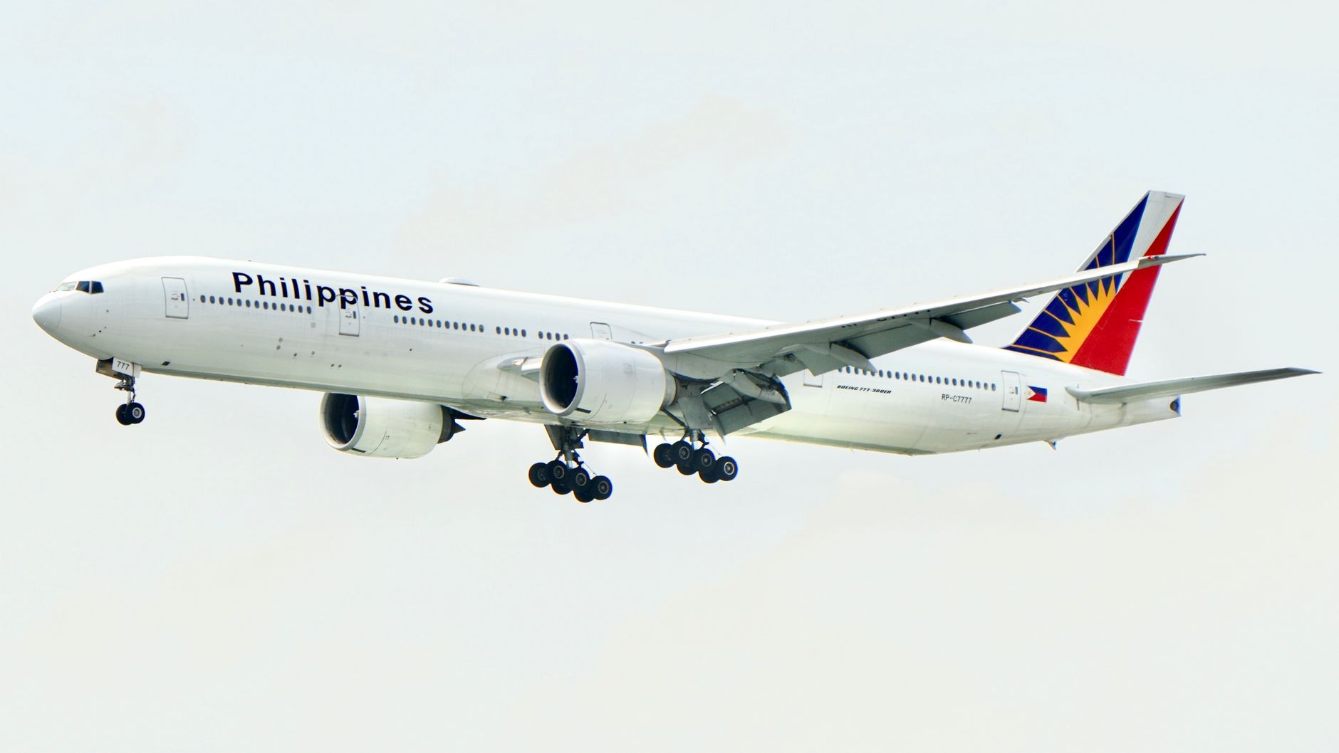 A Philippine Airlines Boeing 777 aircraft flying with landing gear lowered against a clear sky.