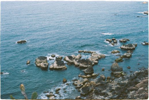 A serene view of a rocky coastline with blue ocean waters and distant waves.