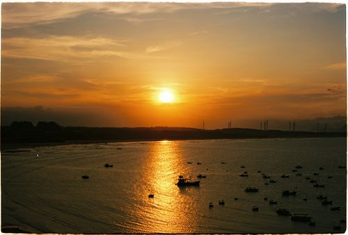Free Golden sunset reflecting on the ocean with scattered boats and distant wind turbines. Stock Photo
