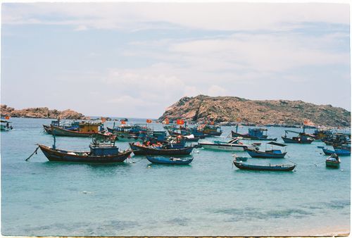 Free Traditional fishing boats anchored in a serene coastal bay against a rocky island backdrop. Stock Photo